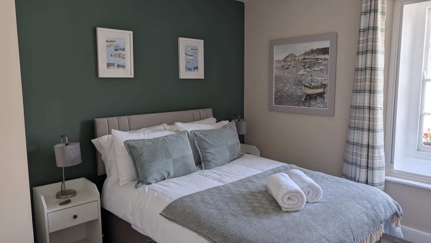 A freshly refurbished double room at The Bugle Inn — dark green feature wall, crisp white linen and Cornish harbour artwork